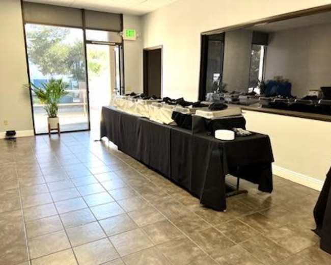 A spacious room with a long table covered in a black cloth, set up for a buffet, and a large window displaying greenery outside.