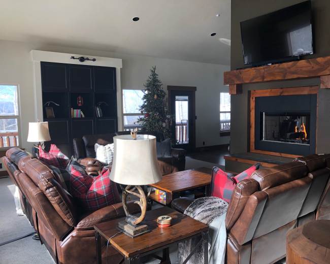 A spacious living room with brown leather sofas, a wooden coffee table, a decorated Christmas tree, and a fireplace with a flat-screen TV above it.