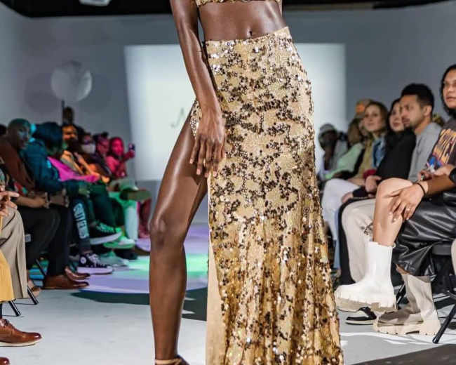 A model walks down a runway in a sparkling gold two-piece outfit during a fashion show.
