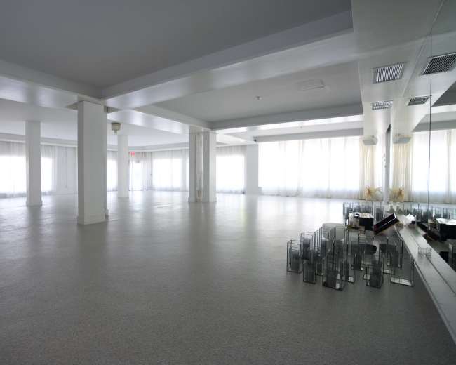 The image shows a spacious, empty room with large windows and a smooth, light-colored floor.
