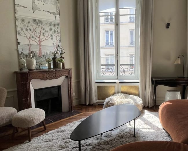 A stylish living room features a curved orange sofa, a circular black coffee table, and large windows allowing natural light to illuminate the space.