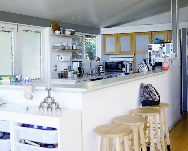 A modern kitchen features a clean design with a central island, bar stools, and shelves displaying dishware and utensils.