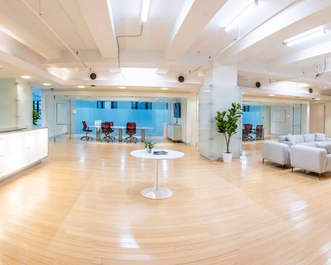 The image shows a modern, open office space with seating areas, conference rooms, and natural light from large windows.