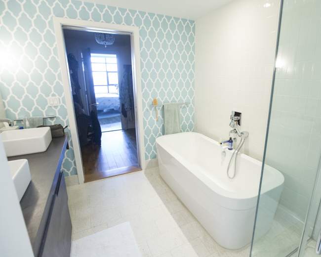 The image shows a modern bathroom featuring a freestanding bathtub, a glass shower enclosure, and a patterned blue wall.