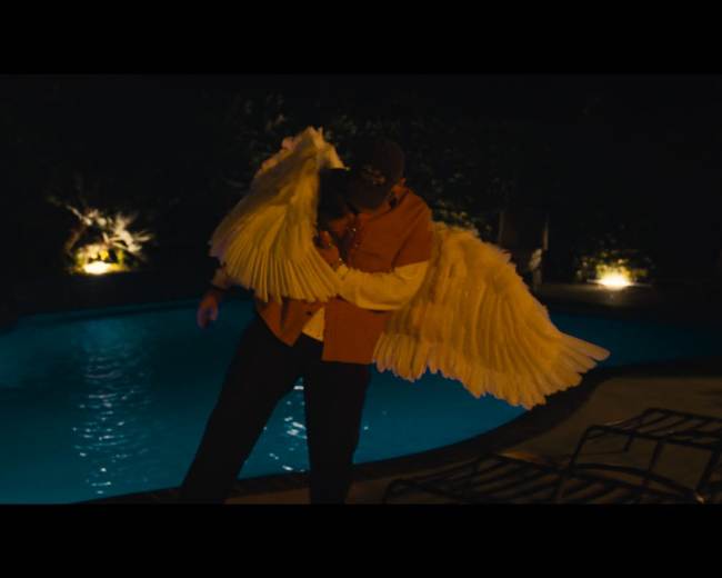 A person wearing large white wings stands by a illuminated pool at night.