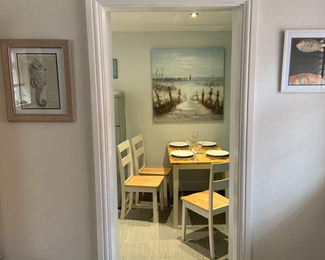 A small dining area features a table with four chairs and a painting of a beach scene on the wall.