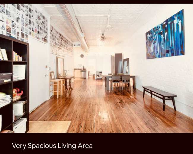 The image shows a large living area with polished wooden floors, white brick walls, and a wall adorned with numerous black-and-white photographs.