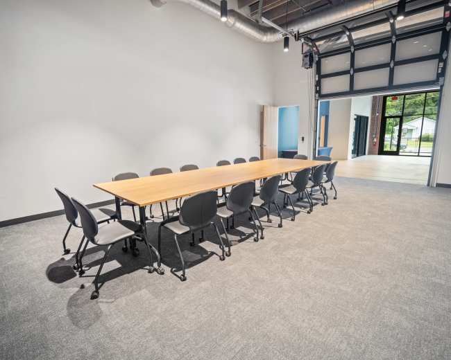 A long wooden table is arranged with ten black chairs on each side in a spacious, empty conference room.