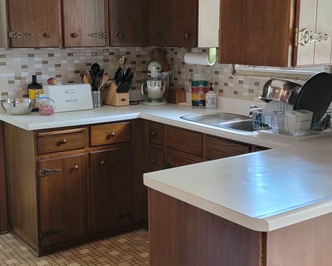 The image shows a kitchen with wooden cabinets, a countertop, and a checkered floor pattern.