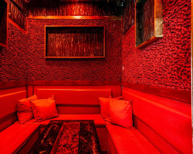 The image shows a small, enclosed seating area with red textured walls and red cushions on benches, illuminated by dim red lighting.