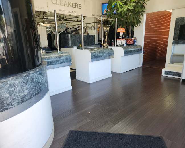The image shows the interior of a dry cleaning business with a reception area featuring multiple service counters and a clean, organized layout.