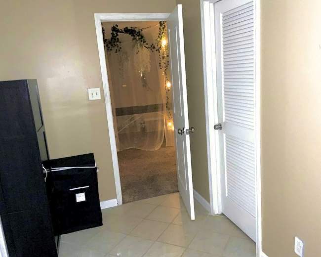 The image shows a doorway with an open door leading to a room, a closed door on the right, and a black container beside the wall.