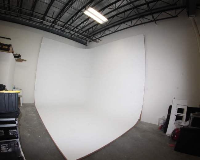 A photography studio with a large white seamless backdrop and various storage containers and equipment along the walls.