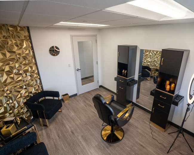 The image shows a modern hair salon interior with a black and gold color theme, featuring a styling chair, mirrors, and a ring light setup.