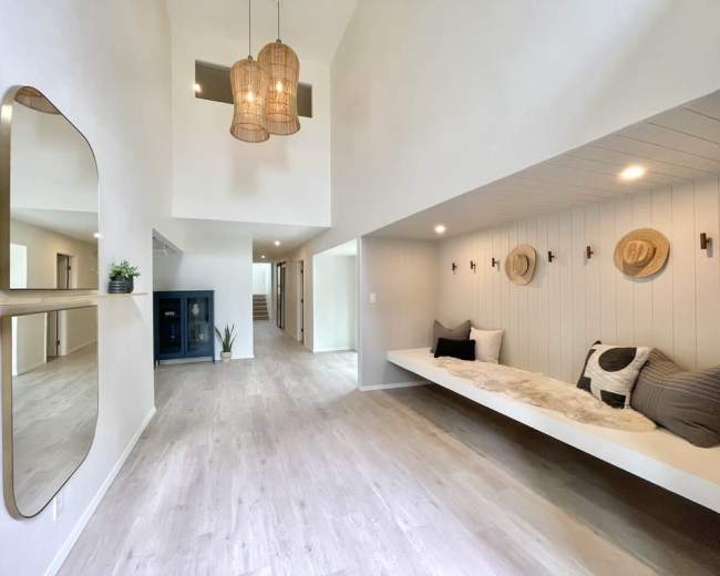 A spacious, modern interior with a seating nook, pendant lights, and a large mirror on one wall.