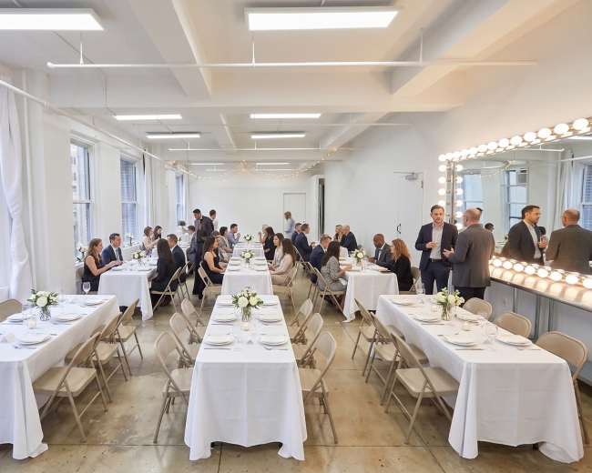 A spacious dining area features elegantly set tables with white linens and centerpieces, accommodating several groups of guests engaged in conversation.