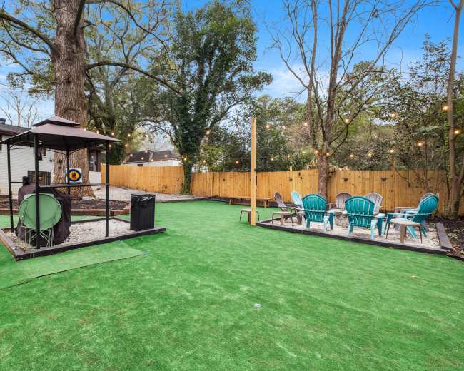 The image shows a backyard with artificial turf, a gazebo with a target, a trash can, and a dining area featuring a table and blue chairs.