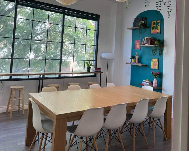 A modern conference room features a large wooden table surrounded by white chairs, with plants adorning the ceiling and shelves.