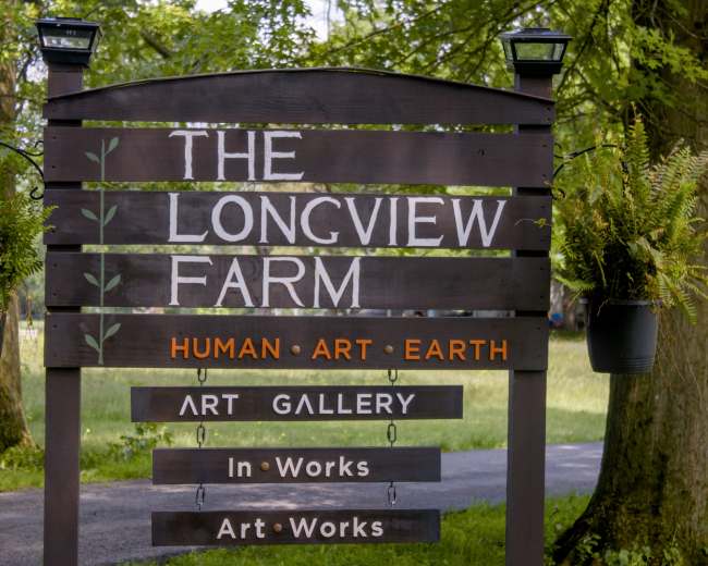 A wooden sign for "The Longview Farm" displays information about its focus on human, art, and earth, along with details about an art gallery.