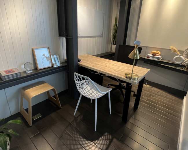 A modern, minimalist office space with a wooden table, a white chair, and decorative elements on the walls and surfaces.