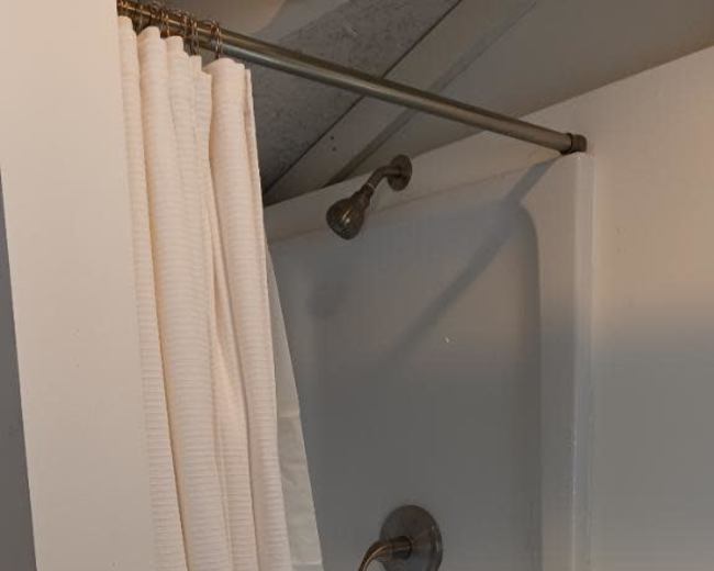 The image shows a shower stall with a white curtain partially drawn, revealing a plain showerhead and faucet.