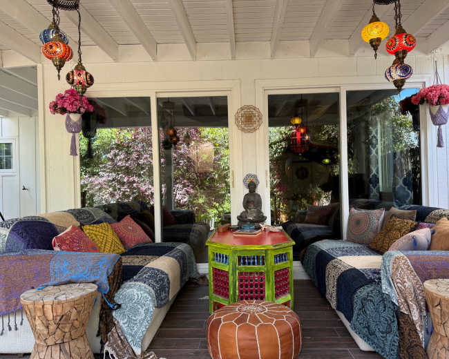 The image shows a cozy outdoor seating area featuring colorful textiles, decorative lanterns, and a statue of Buddha on a vibrant table.