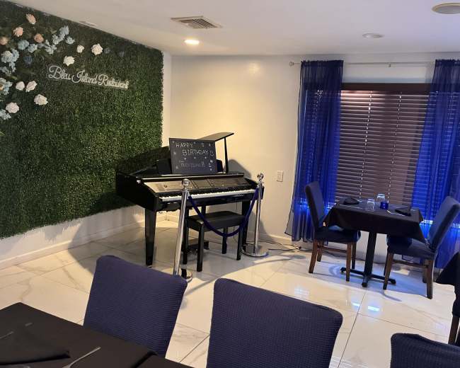 A birthday setup features a keyboard and microphone on a stand next to elegantly arranged tables in a restaurant.