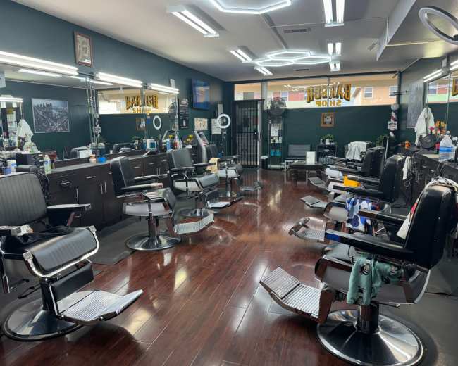 The image shows an empty barbershop featuring several black barber chairs arranged around a central area with mirrors and styling tools visible on countertops.