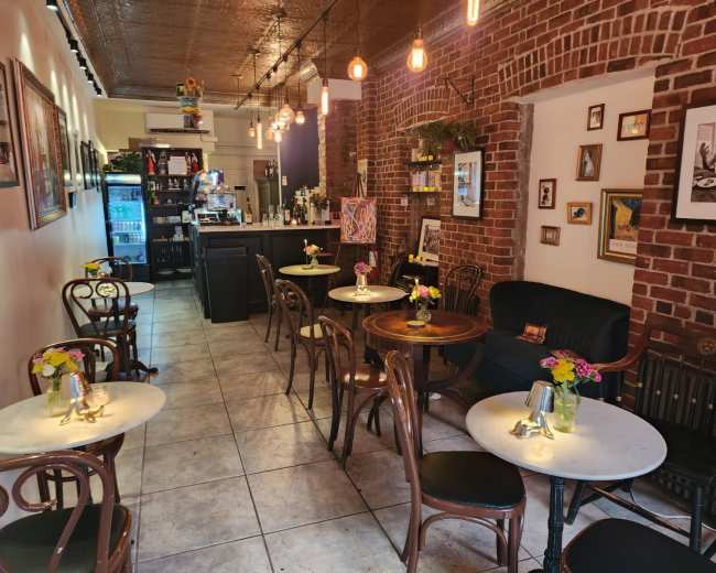 The image shows a cozy café interior with brick walls, small tables adorned with flower vases, and a counter in the background.