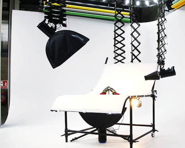 The image shows a photography setup with white backdrop, lighting equipment, and a raised platform on a wheeled frame.