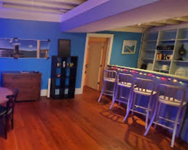 A room with blue walls, a round dining table with chairs, a bar area with stools, and a large window featuring a seaside view.