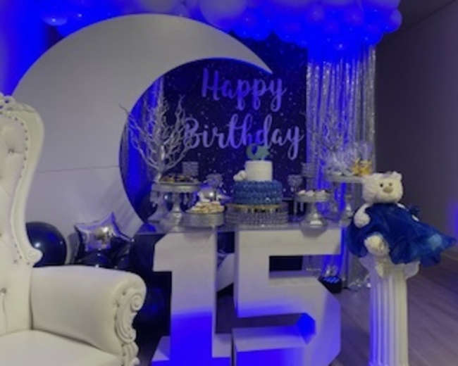 The scene features a colorful birthday celebration setup with a large "15" display, a decorated cake, and a backdrop of balloons and a sparkling sign that reads "Happy Birthday."