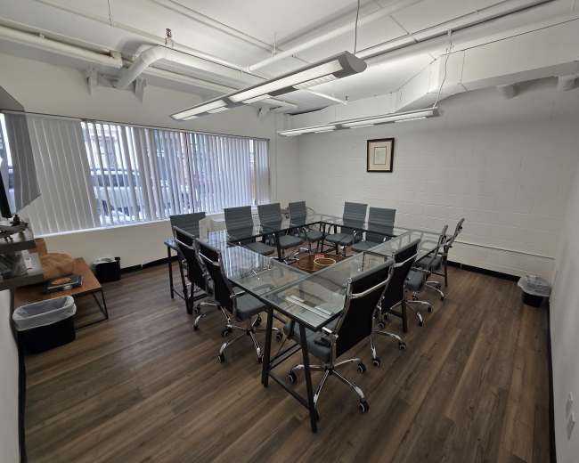 A clean, modern conference room features a glass table surrounded by ergonomic chairs and large windows letting in natural light.