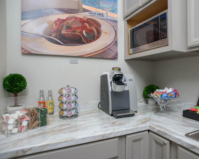 A corner kitchenette features a coffee machine, a microwave, and a selection of beverages and snacks displayed in organized containers.