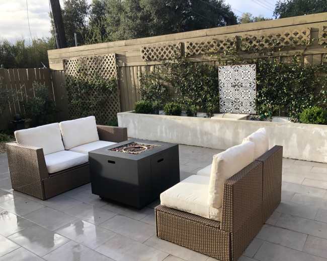The image shows a patio area featuring two chairs and a fire pit surrounded by a decorative wall and plants.
