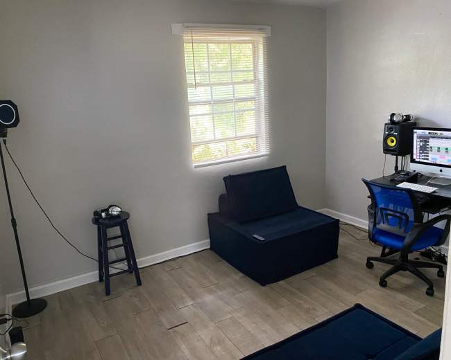 The image shows a small room with a computer desk, a blue chair, a couch, and a standing lamp.