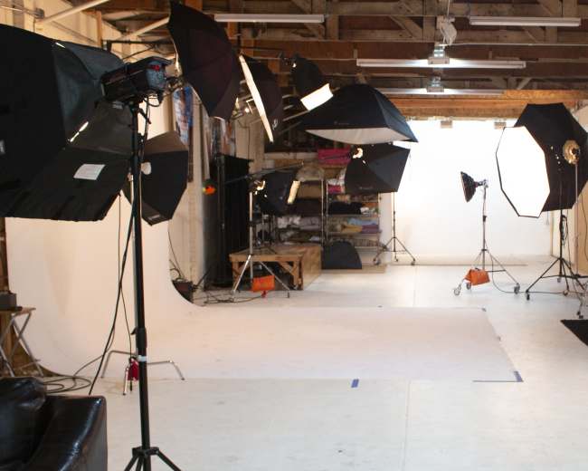 The image shows a photography studio with multiple light setups, backdrops, and a large open space for shooting.