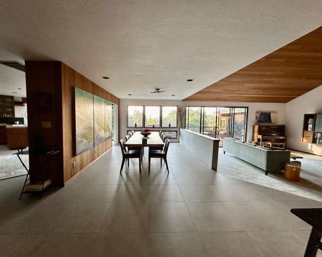 A spacious, modern living area with a dining table, large windows, and sleek furniture.