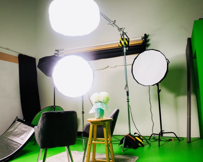 A photography studio setup features softbox lights, a small table with a vase of flowers, and a green backdrop.
