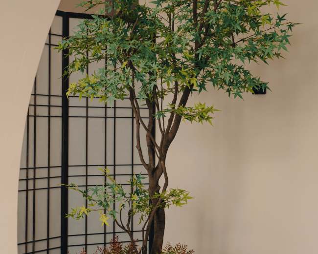A small artificial tree is placed in a gravel and moss garden, surrounded by white stones and a decorative stone lantern.