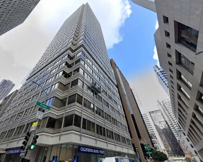 A tall office building with a glass facade is situated at the intersection of streets in an urban environment, surrounded by other skyscrapers.