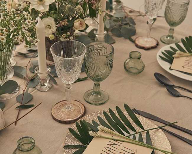 The table is set with various glassware, candles, and leafy decorations, featuring a thank you card placed on a decorative plate.