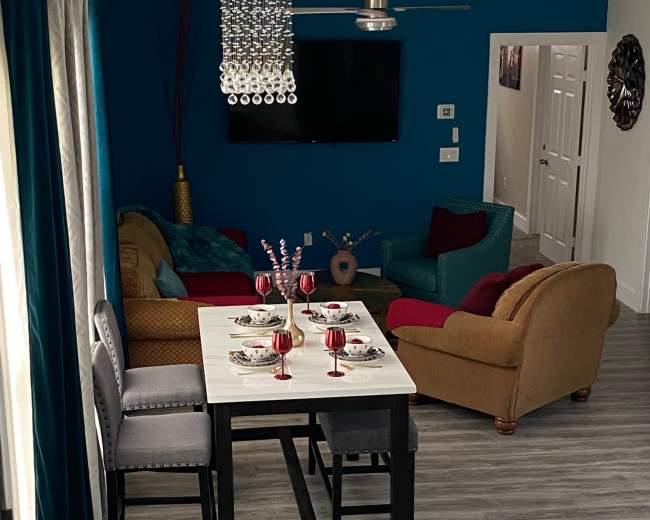 A modern living and dining area featuring a table set for four, a television on the wall, and colorful furniture arrangements.