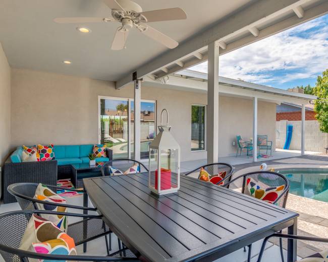 The image shows an outdoor patio area with a dining table, chairs, and a swimming pool, surrounded by trees and a wall.