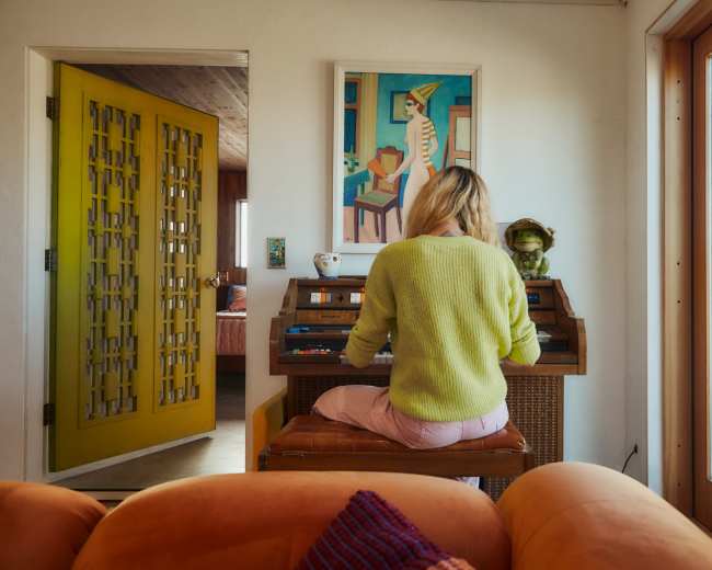 A person sits at an electric keyboard in a brightly colored room with a view of the outdoors.