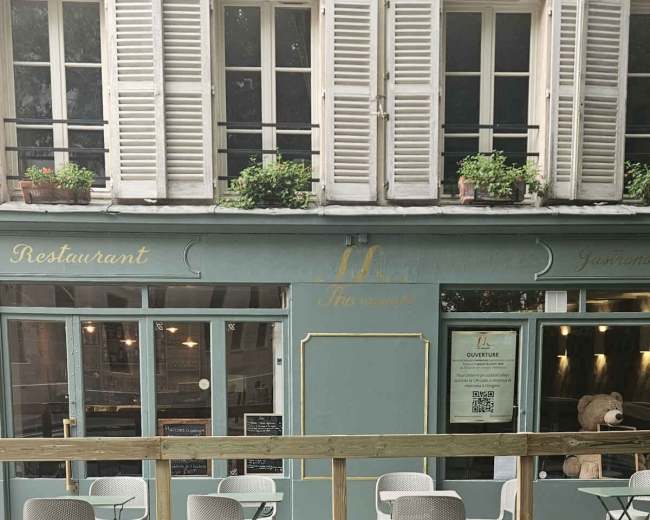 A restaurant with outdoor seating and large windows is situated on a city street, featuring wooden barriers around the seating area.