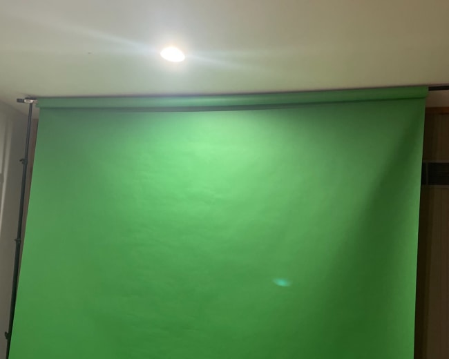 A green backdrop, typically used for chroma keying, illuminated by a ceiling light.