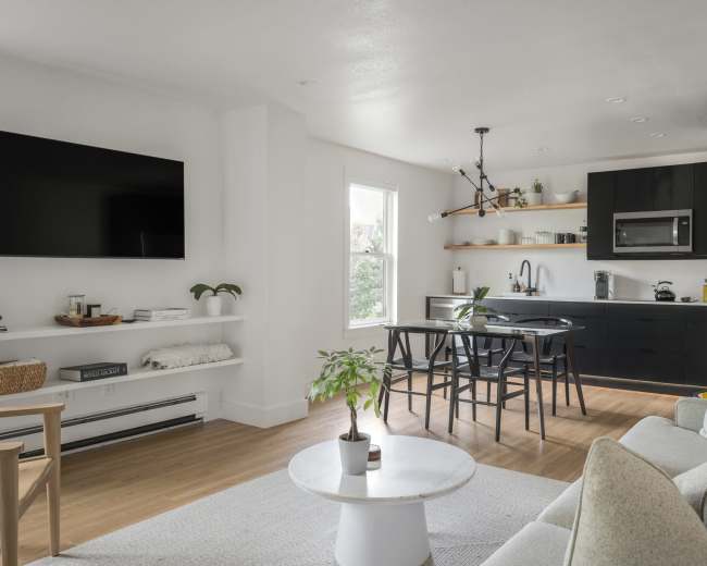 A modern, open-concept living space featuring a living area with a television, a sleek kitchen, and a dining area with a circular table and chairs.
