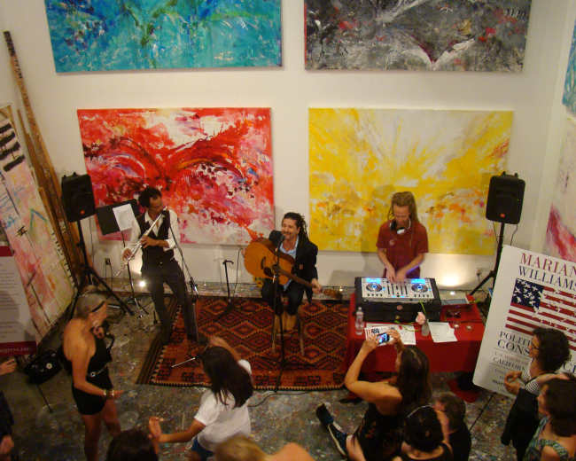 A band performs in an art gallery filled with colorful paintings while a crowd gathers to enjoy the music.