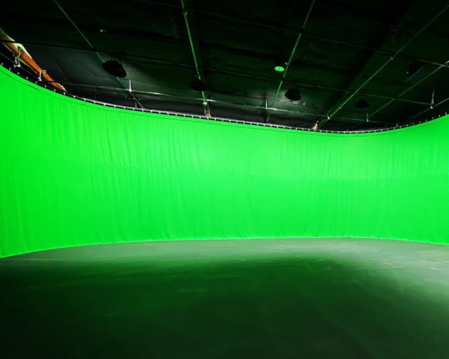 A curved green screen in a studio setting, with black walls and ceiling.